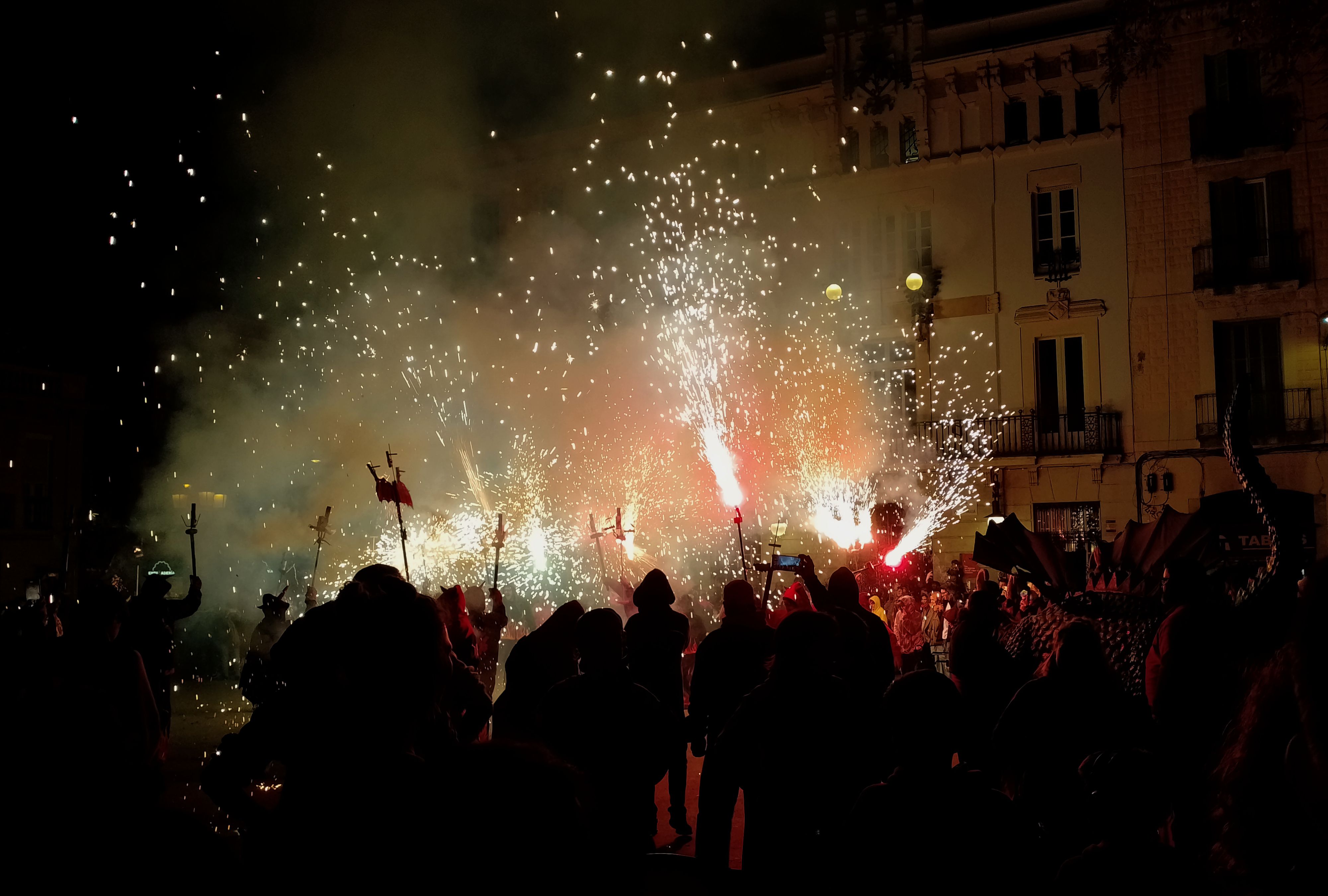 "Photo of the central plaza of Gràcia neighbourhood during the final act of the correfoc. There are dragons, and fire, and lightning sparkles shooting up the height of the 4 story buildings of the plaza