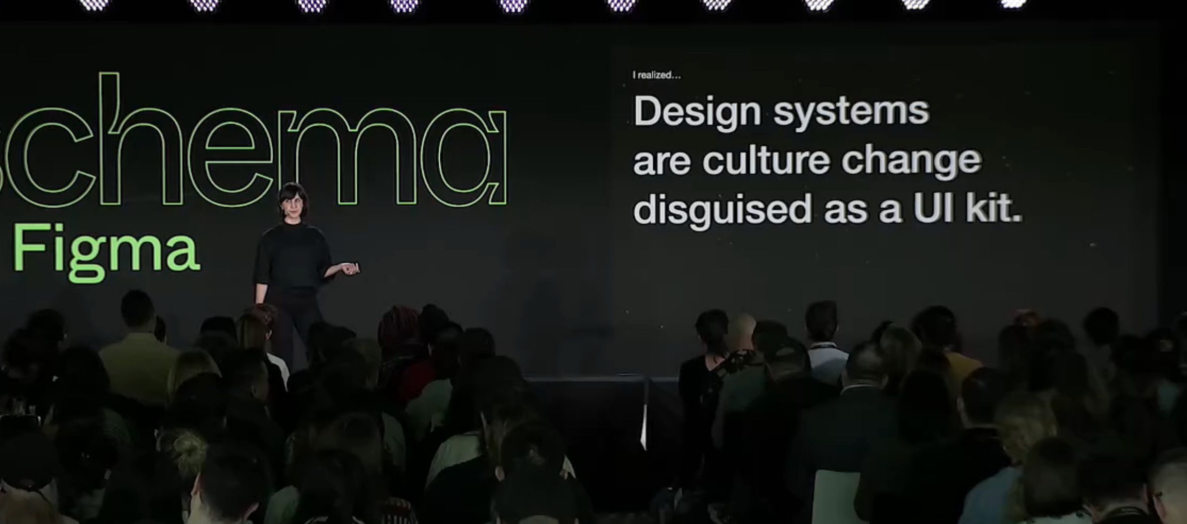 Photo of Lauren LoPrete on stage during Schema 2022, in front of a slide that reads 'Design Systems are culture change disguised as a UI kit'