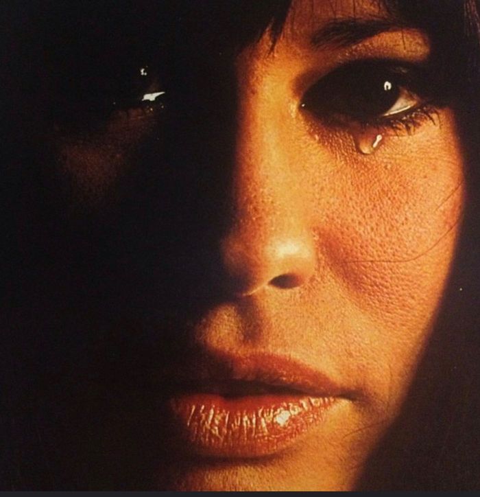 Close up photo of Astrud Gilberto face, in warm light, and dark shadows. Tears are falling from her eyes