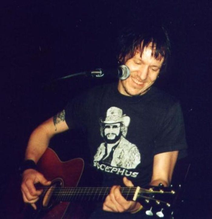 Photo of Elliott Smith playing guitar and smiling on stage.