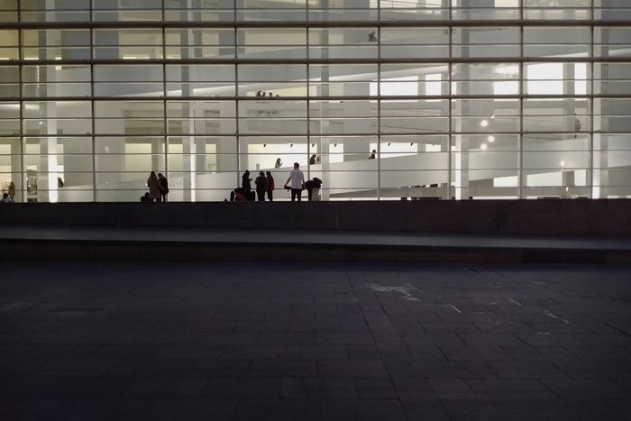 Photo of MACBA plaza by night. The museum is all lit up. The dark stone floor in the plaza is as smooth as you want it to be if you like to skate.