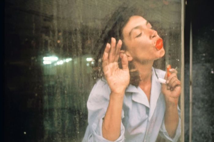 Photo of the artist performing behind a dirty window, kissing the glass with red lipstick lips