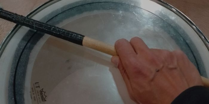 Photo of a hand holding a drumstick against a tom drum.